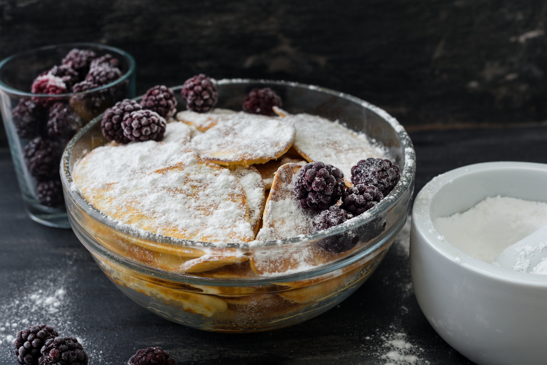 Overhead flat-lay of all ingredients for Austrian Alpine Kaiserschmarrn with Blueberry Compote laid out on a kitchen surface.