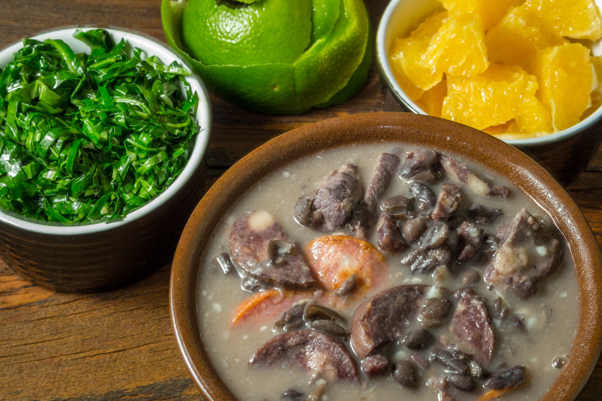 Overhead flat-lay of all ingredients for Brazilian Feijoada with Orange and Collard Greens laid out on a kitchen surface.