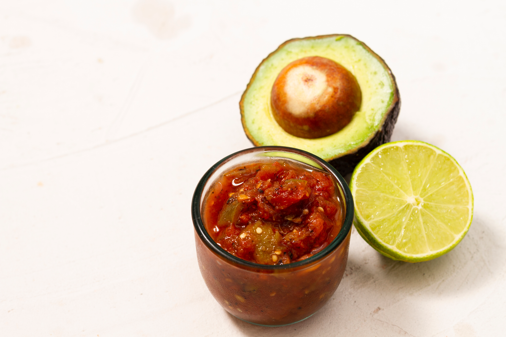Overhead flat-lay of all ingredients for Chilean Pebre Sauce with Hass Avocado and Fresh Lime laid out on a kitchen surface.