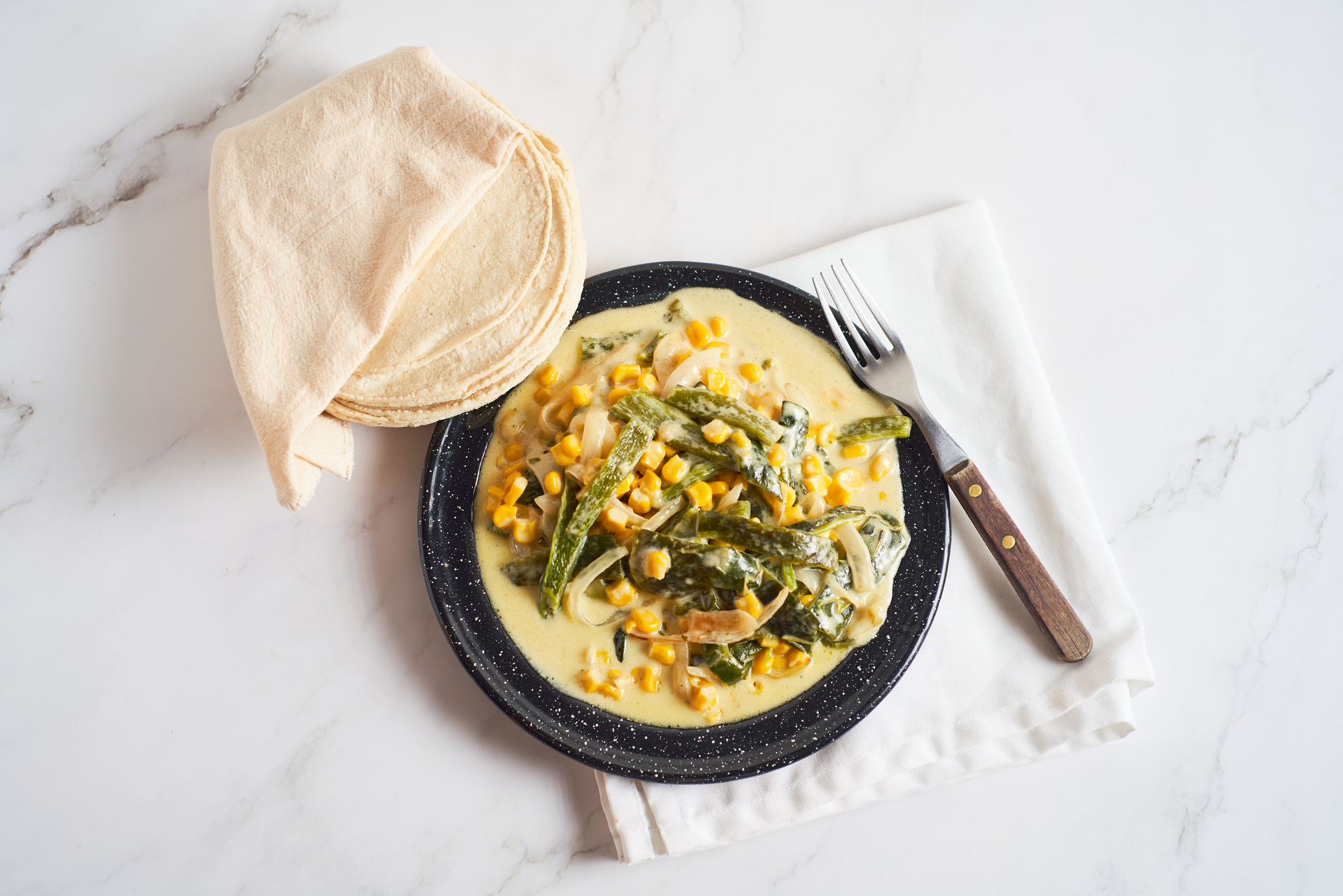 Overhead flat-lay of all ingredients for Creamy Chilean Pastel de Choclo with Sweet Corn and Basil laid out on a kitchen surface.