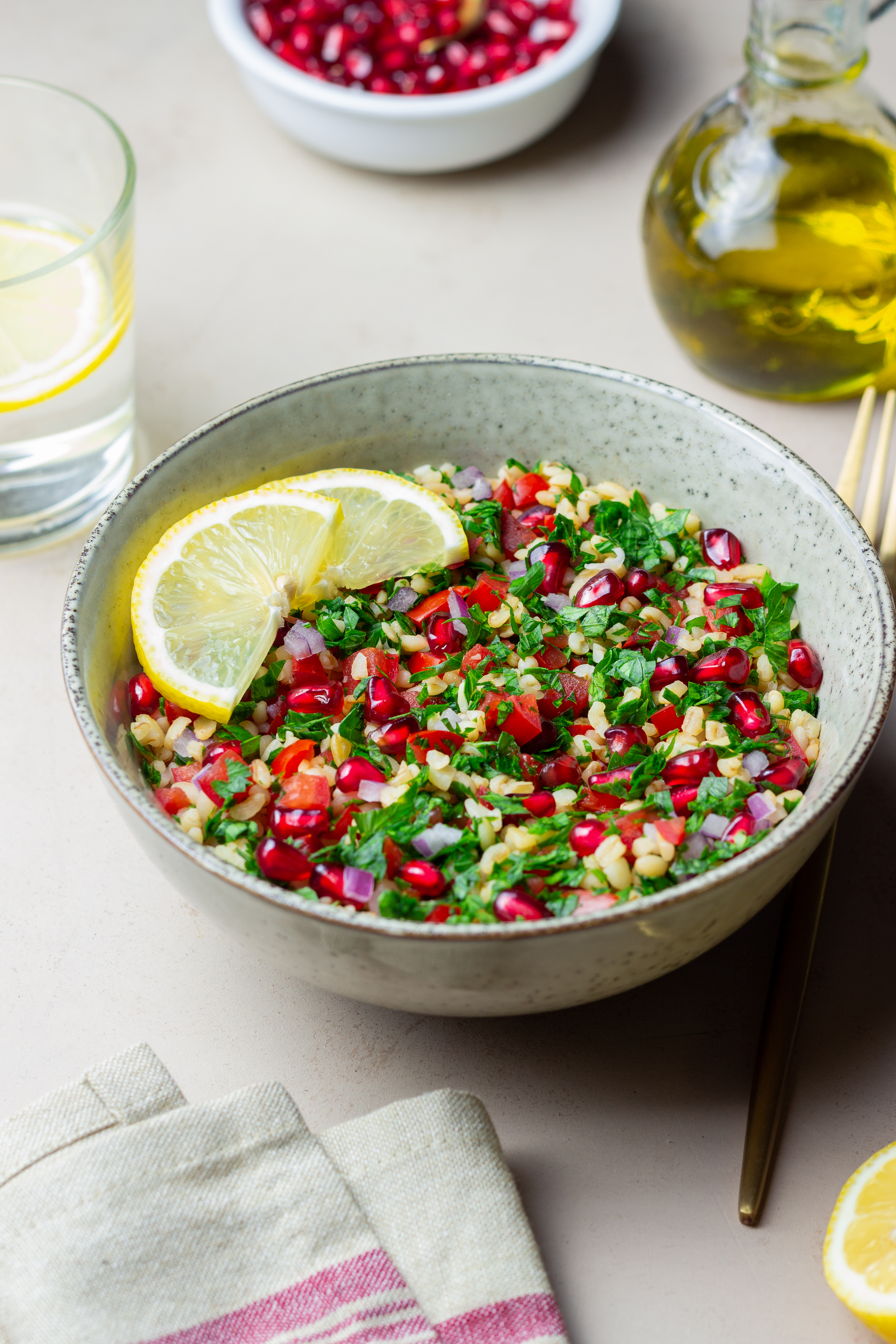 Overhead flat-lay of all ingredients for Crunchy Lebanese Freekeh Salad with Pine Nuts and Pomegranate laid out on a kitchen surface.