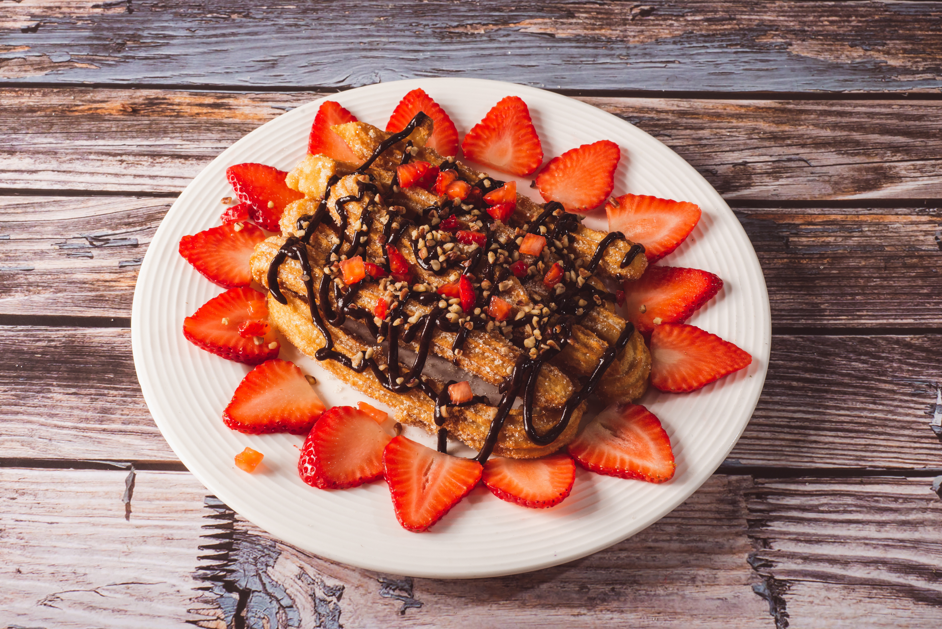 Overhead flat-lay of all ingredients for Decadent Belgian Waffle with Chocolate Sauce and Strawberries laid out on a kitchen surface.