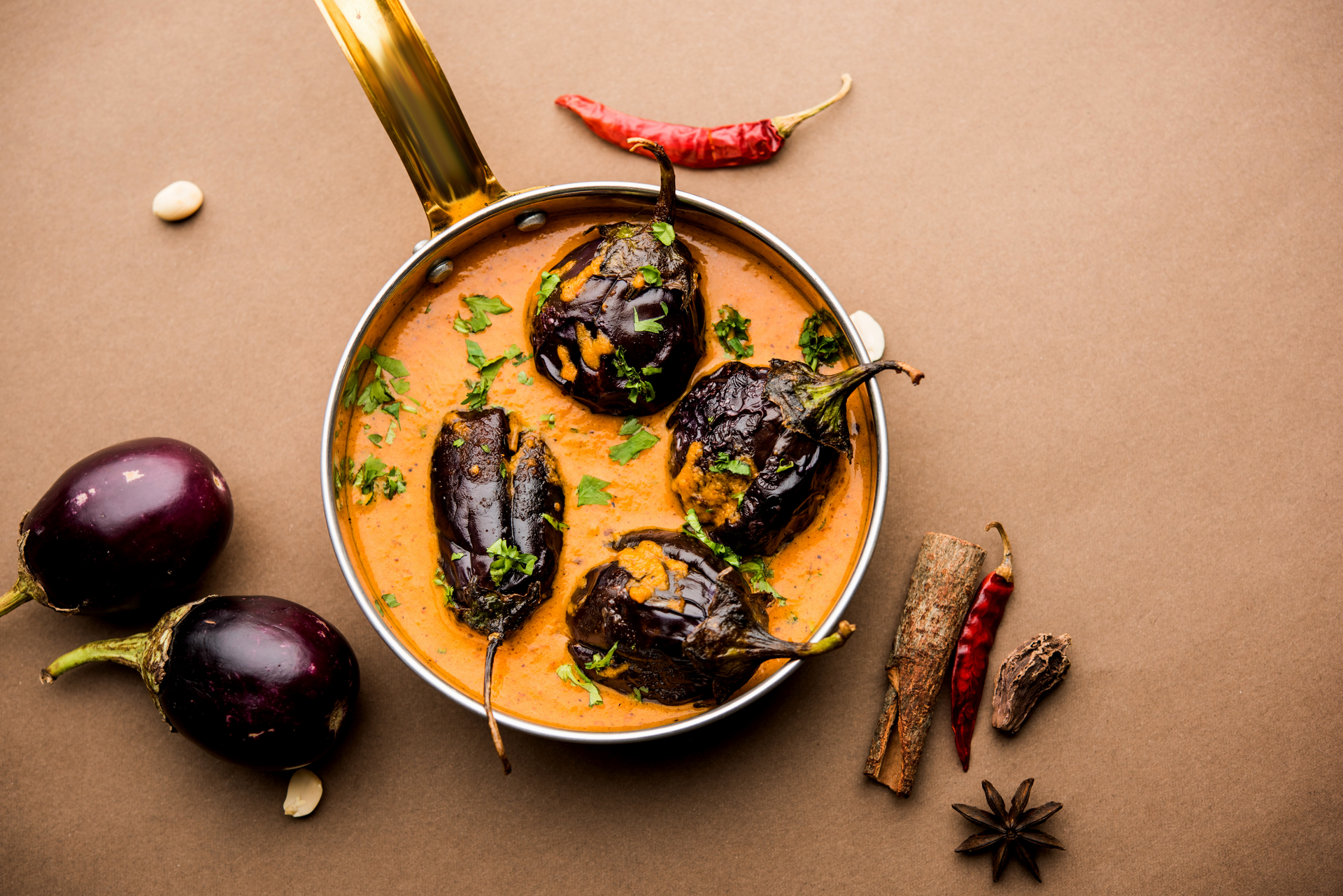 Overhead flat-lay of all ingredients for Earthy Indian Baingan Masala laid out on a kitchen surface.