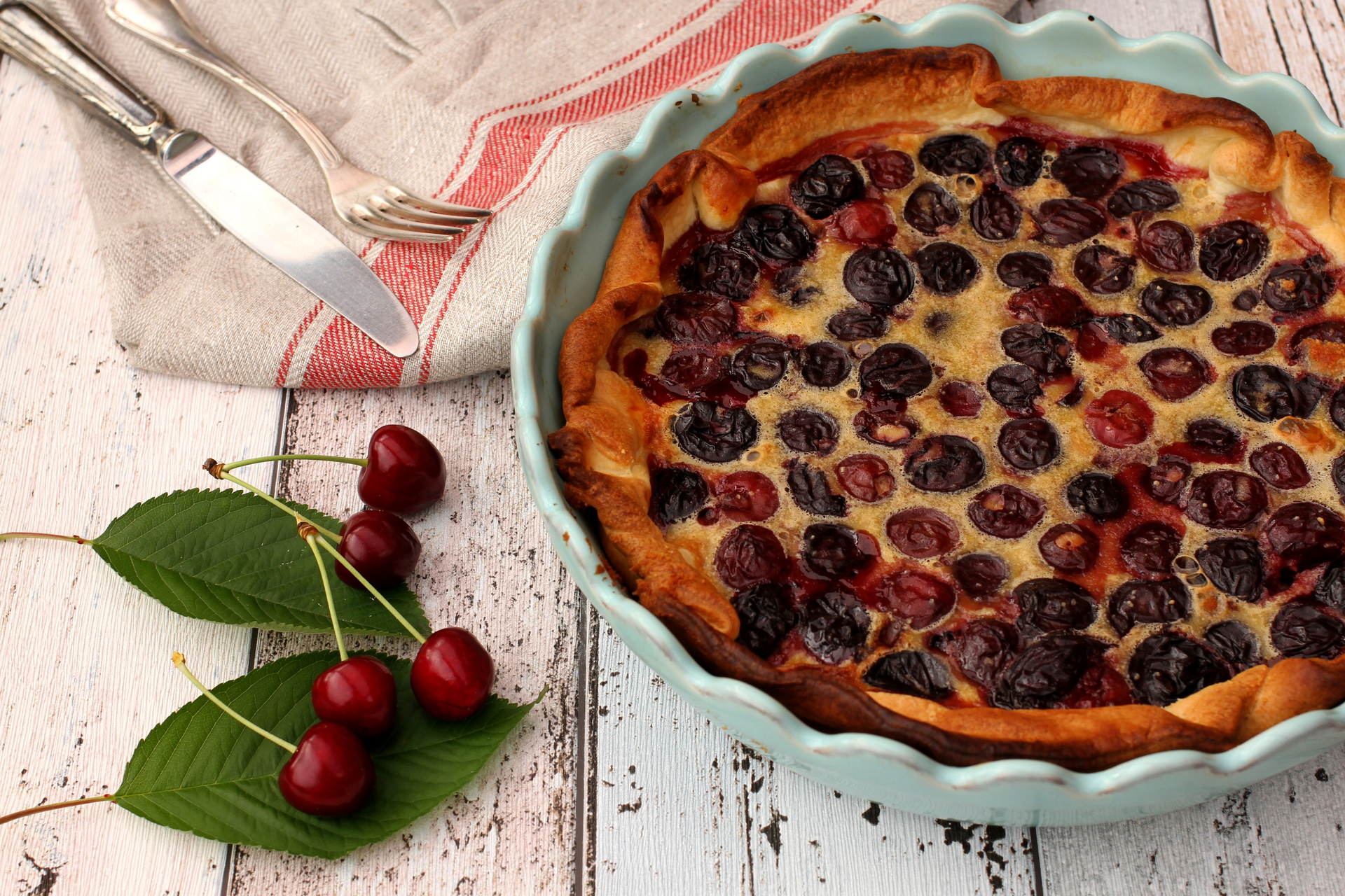 Overhead flat-lay of all ingredients for Elegant French Clafoutis with Cherries and Almonds laid out on a kitchen surface.