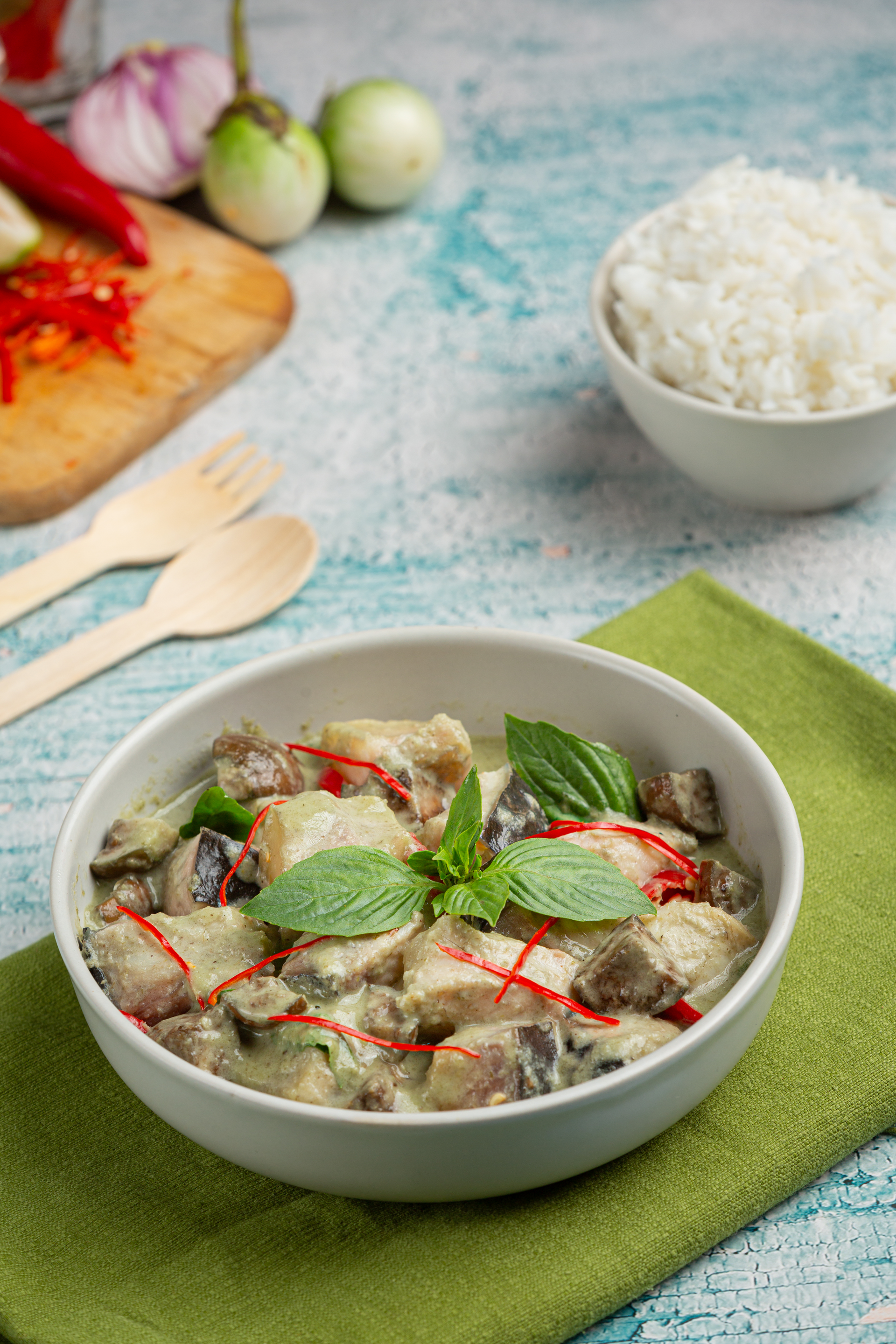 Overhead flat-lay of all ingredients for Fragrant Thai Green Curry with Eggplant and Basil laid out on a kitchen surface.