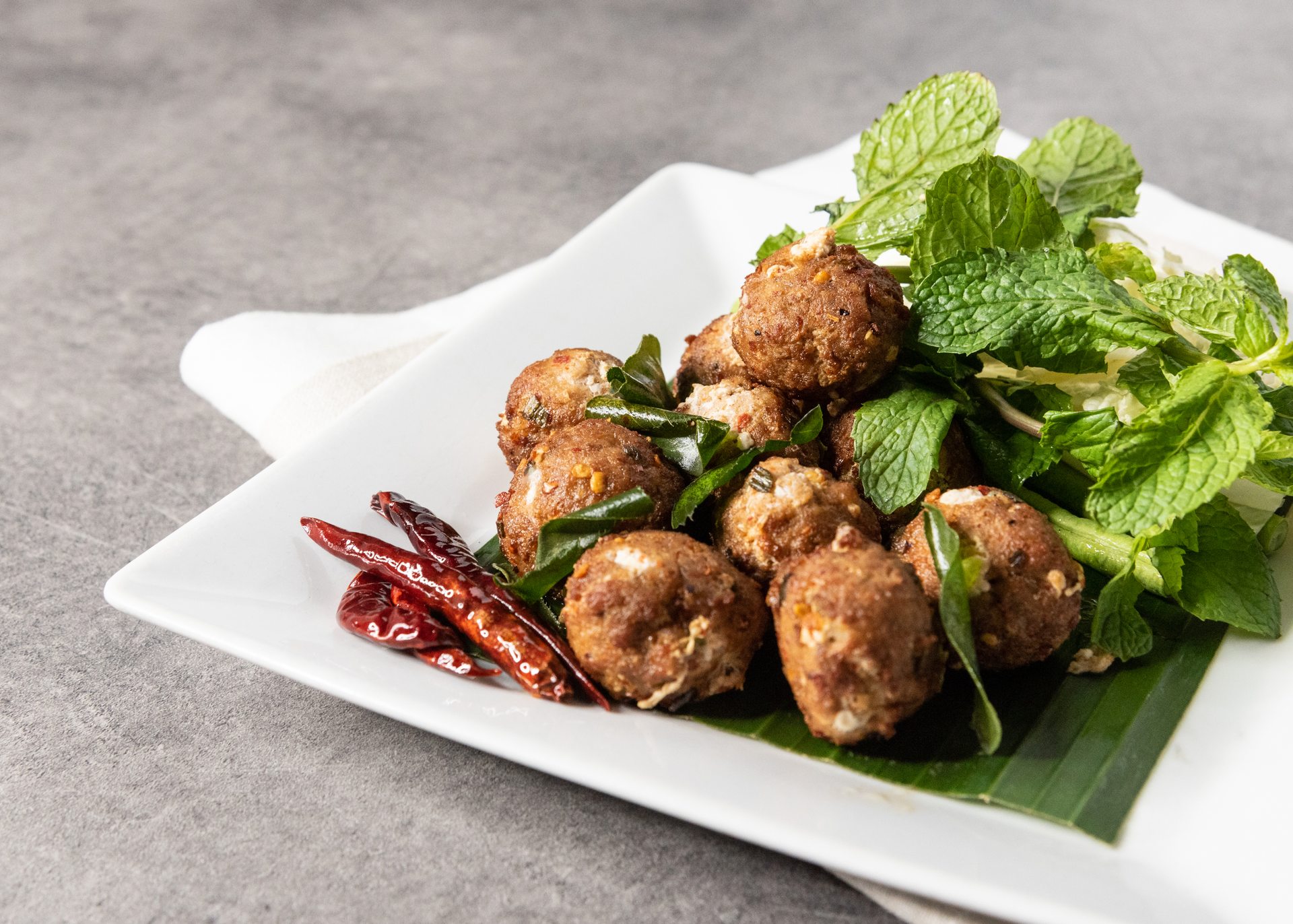 Overhead flat-lay of all ingredients for Honey-Ginger Lao Meatballs with Kaffir Lime Leaves laid out on a kitchen surface.