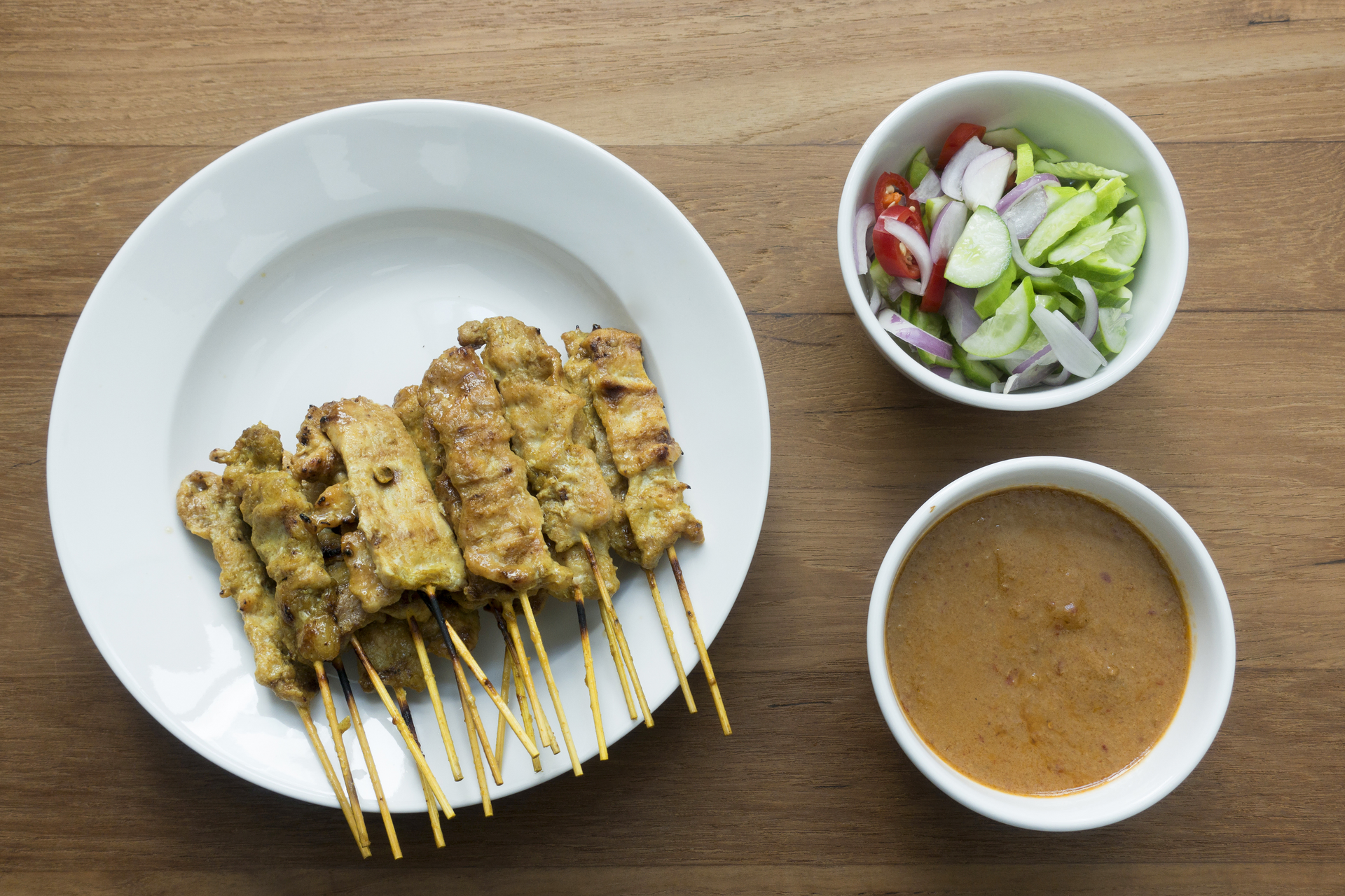 Overhead flat-lay of all ingredients for Indonesian Grilled Tempeh Satay with Spicy Peanut Sauce laid out on a kitchen surface.