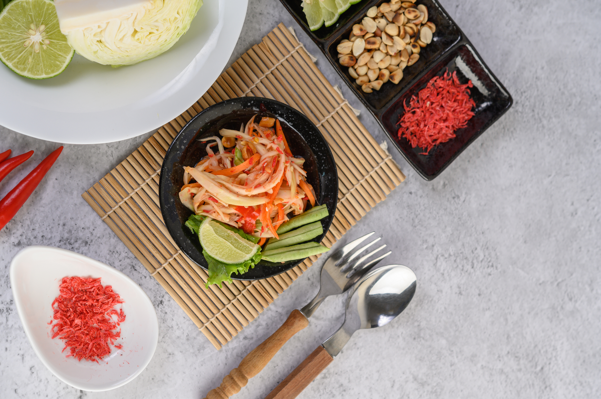 Overhead flat-lay of all ingredients for Refreshing Thai Som Tam laid out on a kitchen surface.