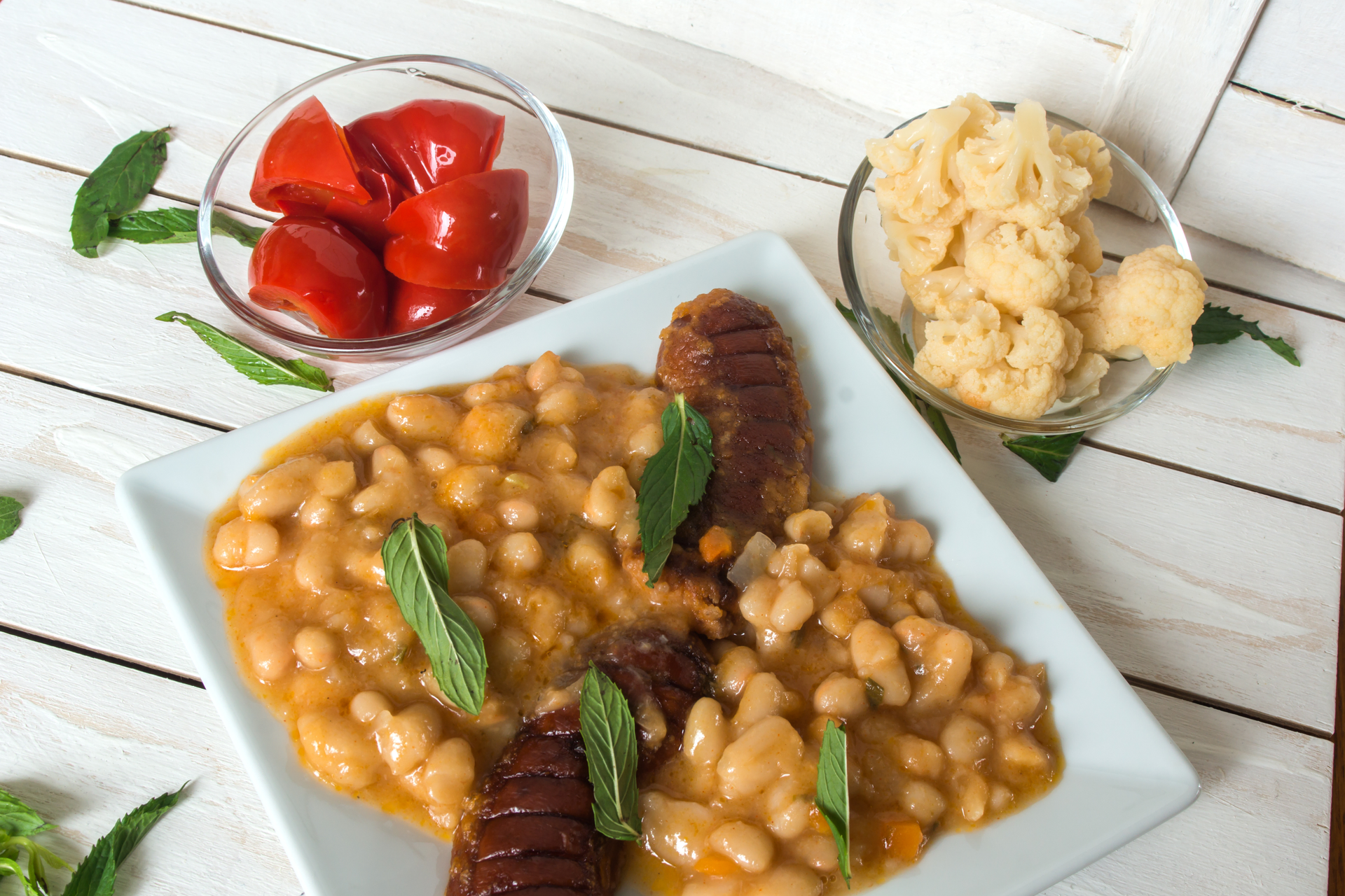 Overhead flat-lay of all ingredients for Rustic Spanish Chorizo Fabada with Cabbage and White Beans laid out on a kitchen surface.