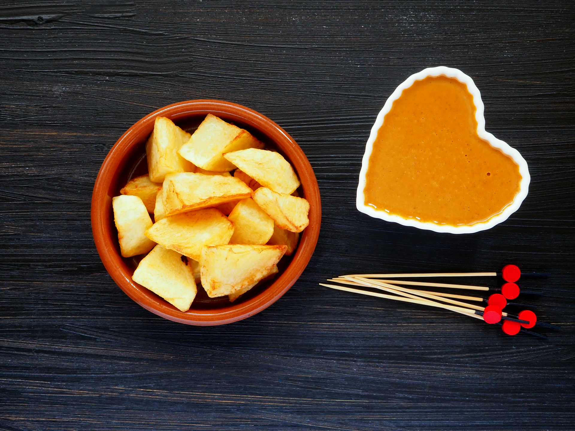 Overhead flat-lay of all ingredients for Spanish Patatas Bravas with Smoky Tomato Sauce laid out on a kitchen surface.