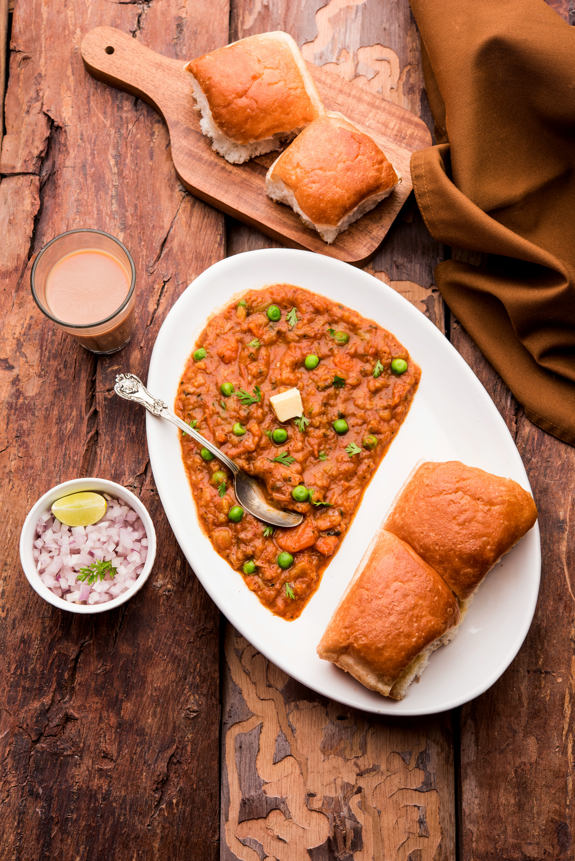 Overhead flat-lay of all ingredients for Spicy Indian Pav Bhaji with Buttered Rolls laid out on a kitchen surface.