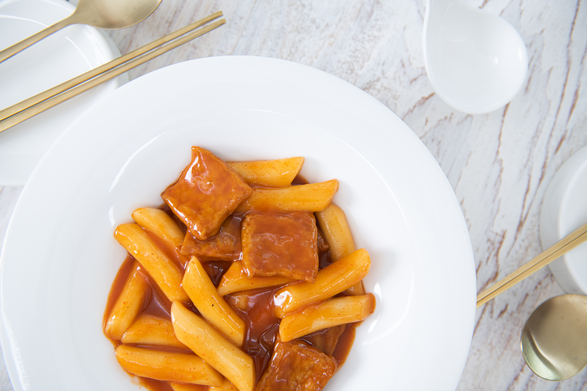 Overhead flat-lay of all ingredients for Spicy Korean Tteokbokki with Fish Cakes laid out on a kitchen surface.