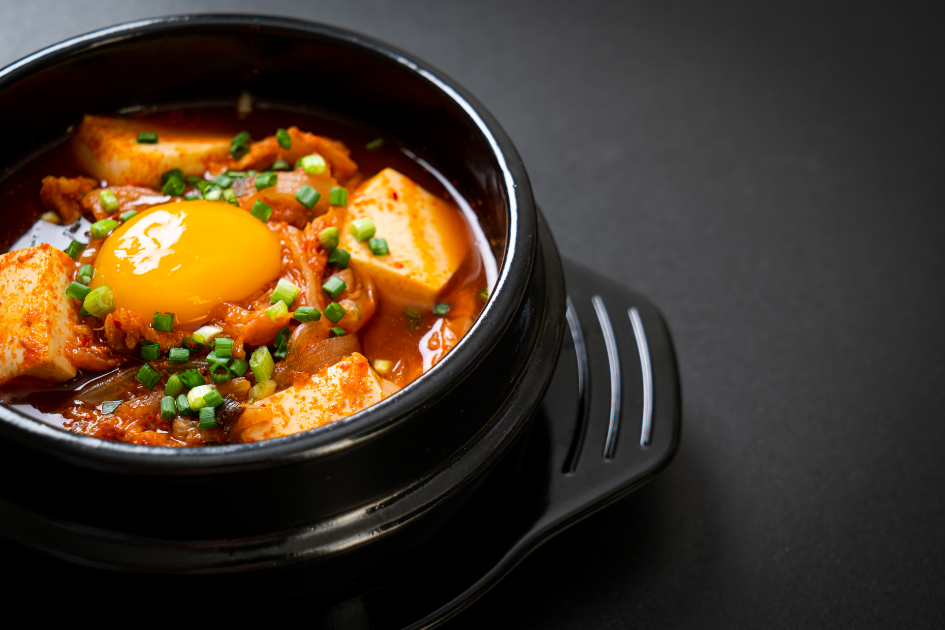 Overhead flat-lay of all ingredients for Sumptuous Korean Kimchi Tofu Stew with Silken Egg Drop laid out on a kitchen surface.