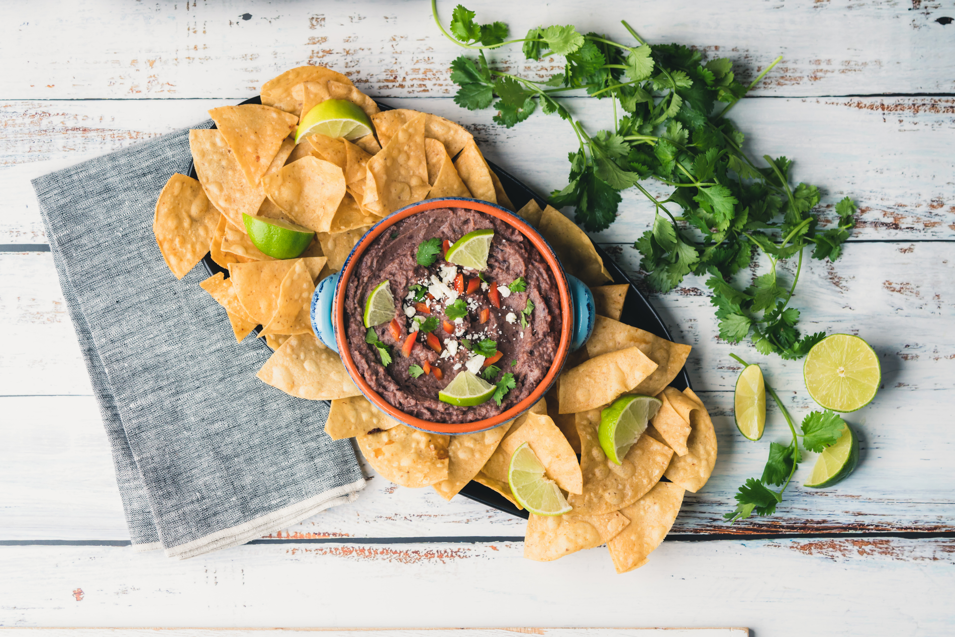 Overhead flat-lay of all ingredients for Zesty Brazilian Feijoada Nachos with Lime Crema laid out on a kitchen surface.